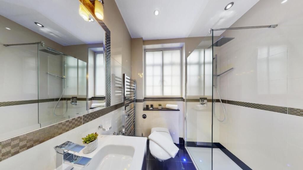 Un baño moderno con cabina de ducha de vidrio, bañera, inodoro y un espejo grande.