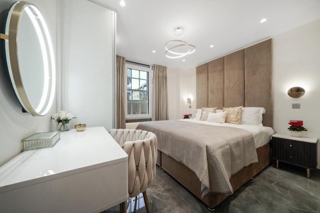 A modern bedroom with a large bed, bedside tables, a vanity with a mirror, and a window with curtains.