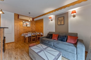 A cozy living room with a grey sofa, wooden dining table, and a box on the floor. - Resort center, floor -1, fitness, swimming pool, sauna, balcony, tv, ski locker, 35m², Les Orres (Les Orres)