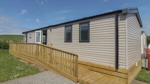A mobile home with a wooden deck, a door, and windows. - The Swift (St Bees)