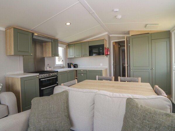 A compact kitchen with a stove, oven, and microwave, a dining table with chairs, and a sofa with cushions.