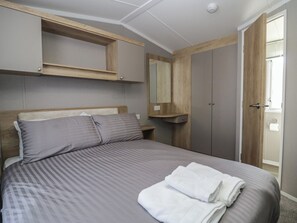 A bedroom with a bed, a wooden headboard, a nightstand, a mirror, and a wardrobe. - The Swift (St Bees)