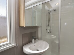 A bathroom with a glass shower enclosure, a white sink, and a mirror above the sink. - The Swift (St Bees)