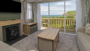 A room with a TV, a wooden table, a sofa, a small desk, a fireplace, and a balcony with a view. - The Swift (St Bees)