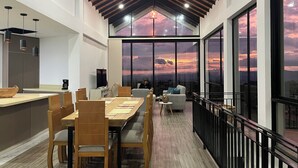 A spacious dining area with a high ceiling and large windows offering a sunset view.