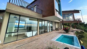 A modern two-story house with large glass windows, a rooftop terrace, and a swimming pool.