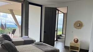A modern hotel room with two beds, a view of the outdoors, a wooden floor, and a small wooden nightstand with a decorative item.