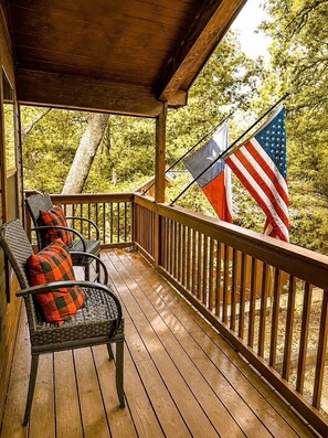 A wooden deck with wicker chairs and a railing, overlooking a forested area.
