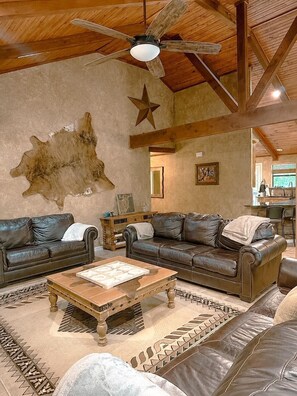 A spacious living room with leather sofas, a wooden coffee table, a ceiling fan, and a large wall-mounted star decoration.