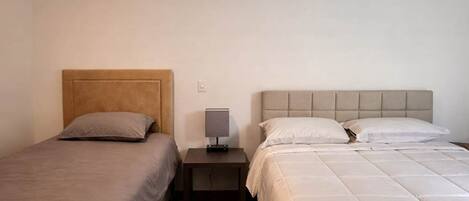 A bedroom with two beds, a nightstand with a lamp, and a wooden floor.