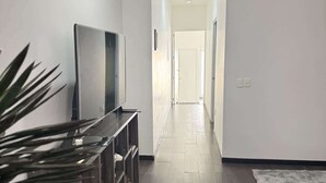 A hallway with a flat-screen TV on a wooden console, a grey rug, and a plant. - Totalmente equipado, Zona Providencia, Apartment (Guadalajara)