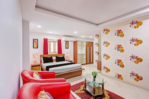 A hotel room with a bed, a red sofa, a glass coffee table, and a wall with a geometric pattern. - Deluxevijaya Residency (Visakhapatnam)