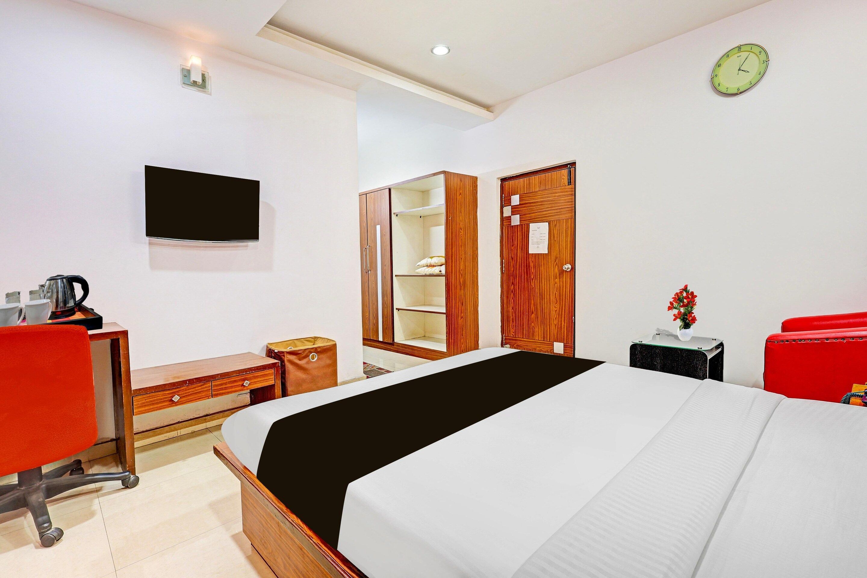 A hotel room with a bed, a desk, a chair, a wardrobe, a TV, and a clock.