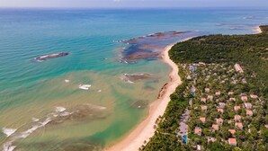 Eine Luftaufnahme einer Küstenregion mit Strand, einem dichten Häuserkomplex und klarem, blauem Wasser.