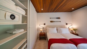 Ein Hotelzimmer mit Holzboden, einem Bett mit weißer Bettwäsche und roten Decken, zwei Nachttischen mit Lampen sowie einer an der Wand montierten Sicherheitsvorrichtung.