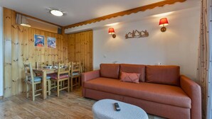 Una stanza con rivestimento in legno, un divano, un tavolo da pranzo con sedie e due lampade a parete.
