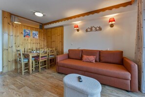 Ein Zimmer mit Holzvertäfelung, einem Sofa, einem Esstisch mit Stühlen und zwei Wandleuchten.
