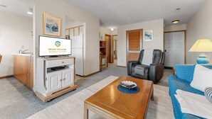 Une chambre d’hôtel équipée d’une télévision, d’un canapé, d’un fauteuil, d’une table basse et d’une lampe.