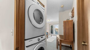 Une buanderie équipée de machines à laver et de sèche-linge superposés, d’un meuble en bois et offrant une vue sur l’extérieur.