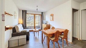 Un salon comprenant un canapé, une table à manger en bois avec des chaises, un téléviseur et une fenêtre avec des rideaux.