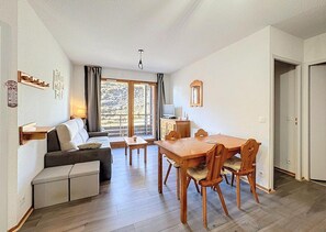 A living room with a sofa, a wooden dining table with chairs, a television, and a window with curtains. - 200m from resort center, 1st floor, swimming pool, balcony, tv, ski locker, 40m², Le Corbier (Le Corbier)