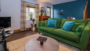 A green sofa, a round table with a candle, a TV, and a window with curtains. - The Green (Ripon)