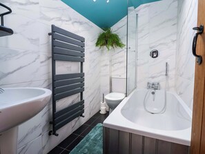 A bathroom with a marble wall, a black towel rack, a white sink, a toilet, and a bathtub. - The Green (Ripon)