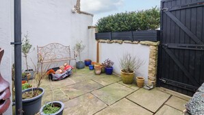 A courtyard with a black gate, potted plants, a metal bench, and a stone wall. - The Green (Ripon)