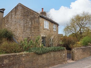 A stone house with a pitched roof, a chimney, and a small garden with a stone wall and plants. - The Green (Ripon)