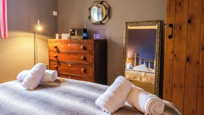 A hotel room with a bed, a wooden dresser, a mirror, and a nightstand with a lamp. - The Green (Ripon)