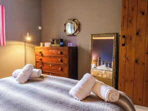 Ein Hotelzimmer mit Bett, einem Holzkasten, einem Spiegel und einem Nachttisch mit Lampe.