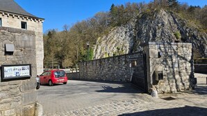 Um edifício de pedra com um carro estacionado na frente, um muro de pedra e um portão.