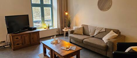 A living room with a television, a sofa, a coffee table, and a window with curtains.