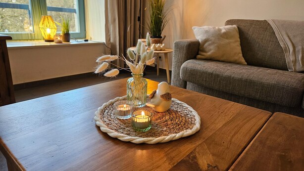 Uma sala de estar aconchegante com uma mesa de centro de madeira, um vaso com plantas secas e uma vela acesa.