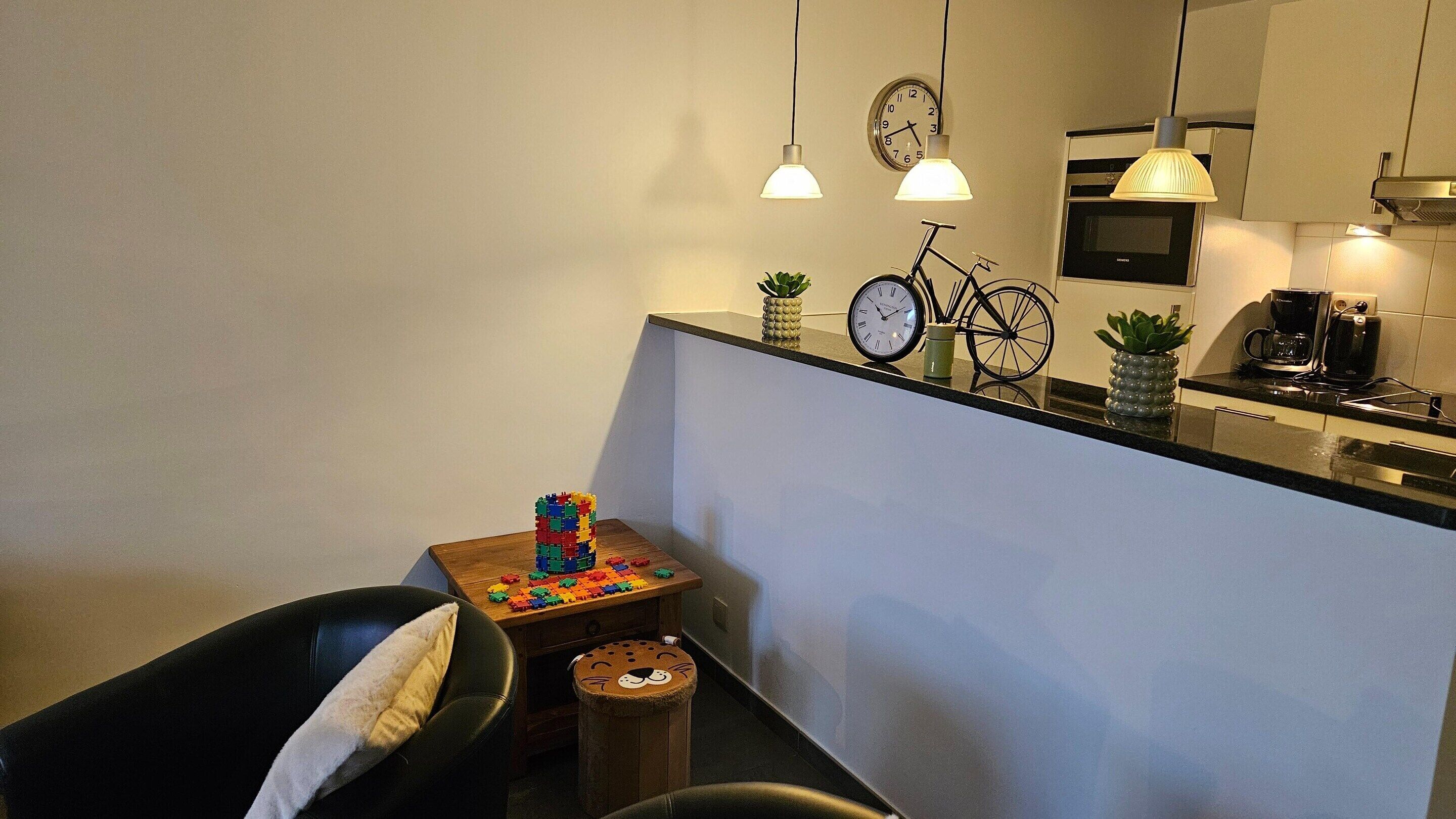 Uma cozinha compacta com área de refeições, com uma mesa de madeira, brinquedos, uma cadeira preta e um banquinho pequeno.