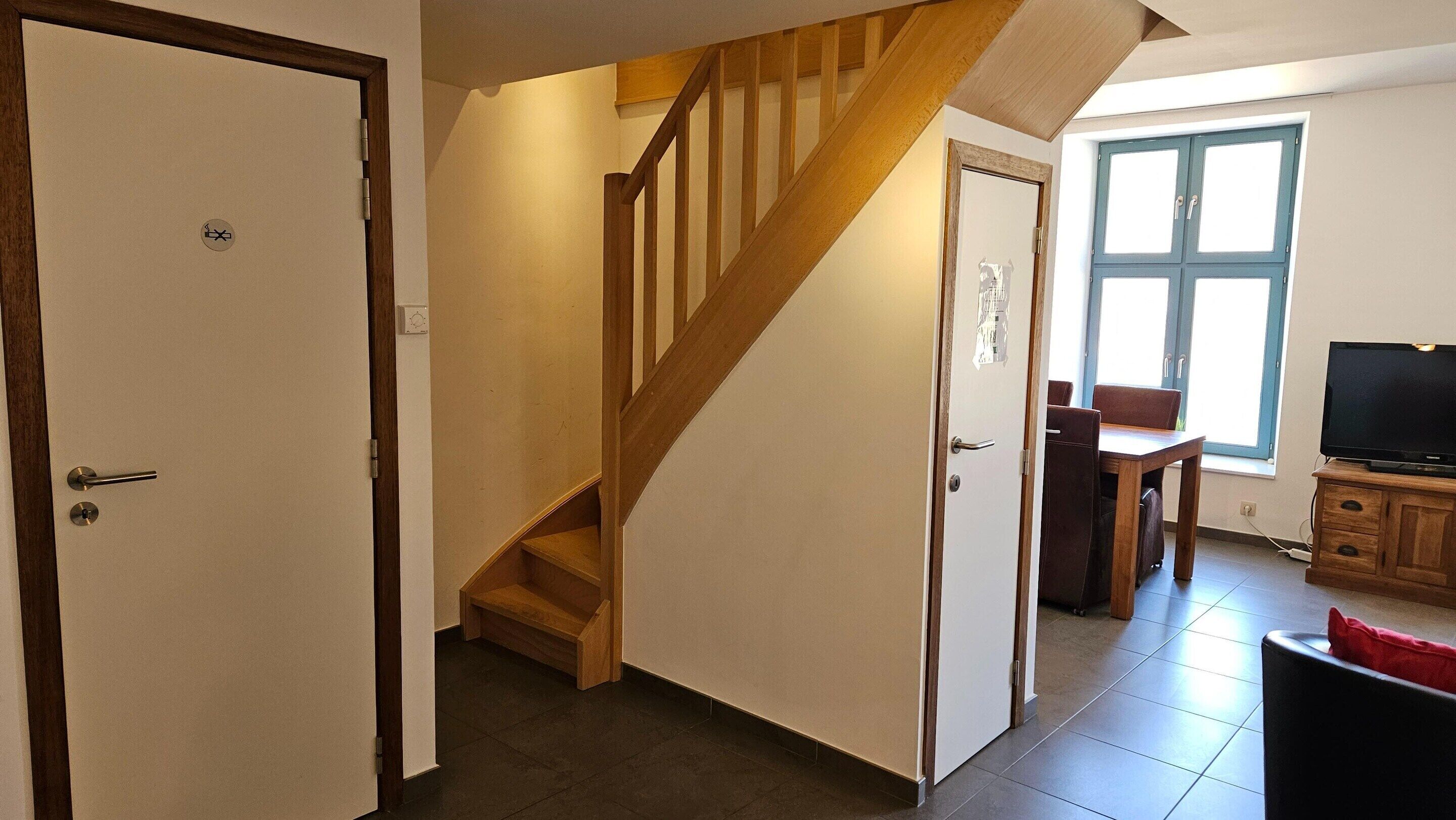 A staircase leading to a second floor, a dining area with a table and chairs, and a television on a wooden cabinet.