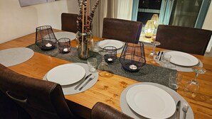 Mesa de jantar posta com pratos brancos, talheres e velas em suportes de arame.