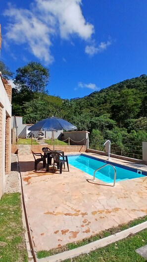 Une piscine dotée d’une terrasse carrelée, d’un espace salon couvert et offrant une vue sur un paysage vallonné.