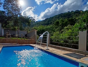 A swimming pool with a water feature, surrounded by a fence and greenery. - Casa da Mata (São Lourenço)