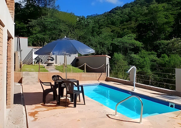 Una piscina con una escalera de metal, rodeada por un suelo de hormigón, con una mesa y sillas, y una tienda de campaña al fondo.
