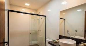 Un baño moderno con ducha acristalada, un lavabo blanco y un espejo grande.