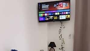 A small, modern room with a white desk, a flat-screen TV mounted on the wall, a lamp, and a chair. - Casa da Mata (São Lourenço)