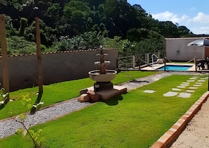 Un patio trasero con piscina, una fuente y un césped bien cuidado.
