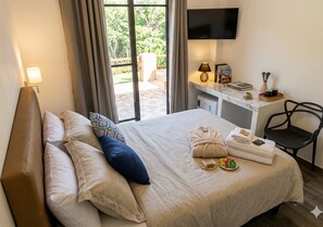 A hotel room with a bed, a desk with a TV, a chair, and a view of the outdoors.