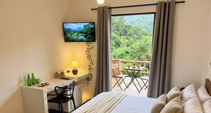 Un dormitorio con cama, escritorio, televisor y balcón con vistas a zonas verdes.