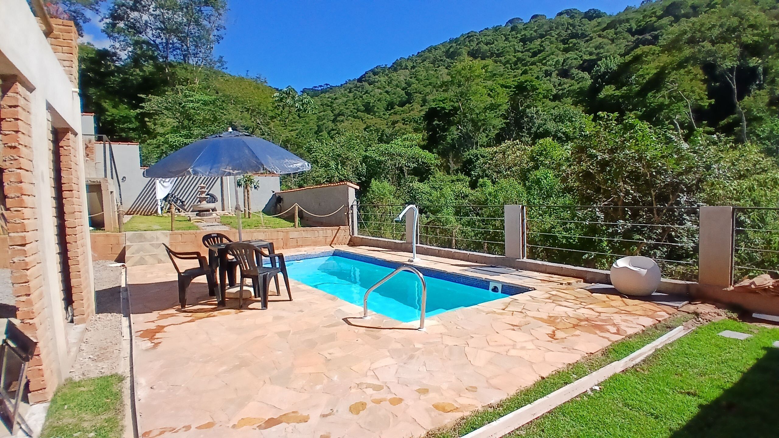Una piscina con un patio de piedra, una mesa con sillas, y un área cubierta con una mesa y sillas.