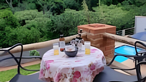 An outdoor patio with a table set for two, surrounded by chairs, a brick oven, and a swimming pool. - Casa da Mata (São Lourenço)