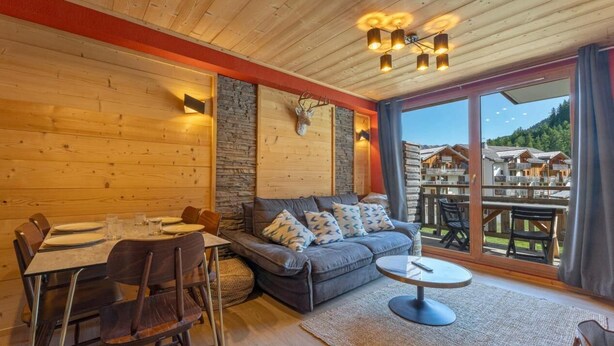 Un interior de madera con una mesa de comedor, sofá y vistas de edificios a través de amplios ventanales.
