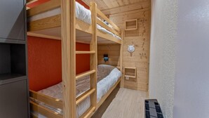 Habitación con literas, techo de madera, pared roja y una pequeña repisa.