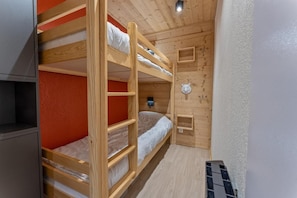 Ein Schlafraum mit Etagenbetten, Holzboden und einer kleinen Ablagefläche. Eine Wand ist rot gestrichen.